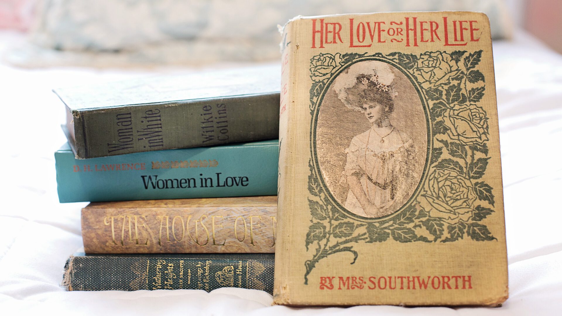 Alte, aufeinander gestapelte Bücher und eines lehnt mit dem Cover nach vorne an dem Stapel. Die Titel haben alle etwas mit Frauen zu tun.