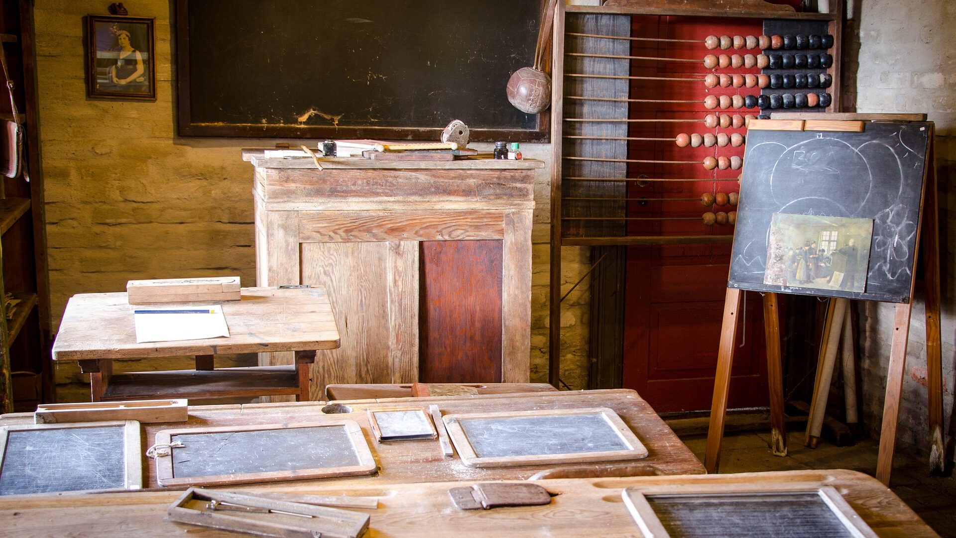 Ein altes Klassenzimmer mit einigen Kreidetafeln auf den Tischn und auf den Wänden, einem Lehrerpult und einem großen Abakus.
