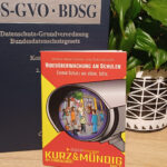 Das Mini-Buch "Videoüberwachung an Schulen" steht in einem regal vor dem Buch "DS-GVO – BDSG". Daneben eine schöne Grünpflanze.