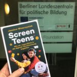 Das Buch „Screen Teens“ wird vor dem Eingang der Landeszentrale für politische Bildung Berlin hochgehalten.